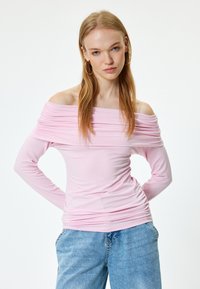 Rosa schulterfreies Langarmoberteil mit gerafften Stoffdetails und taillierter Silhouette, kombiniert mit hellblauen Jeans.