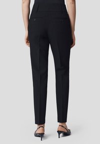 Czarne dopasowane spodnie o wąskim kroju, z dwoma tylnymi kieszeniami i gładką teksturą, zestawione z czarnymi klapkami na wysokim obcasie.