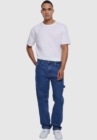 Camiseta blanca de algodón combinada con vaqueros de denim azul; los vaqueros tienen bolsillos laterales y un ajuste holgado; completado con zapatillas blancas.