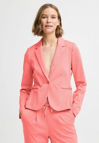 Korálový blazer vyrobený z mäkkej látky, s priliehavým strihom, klopovými goliermi, jedným gombíkom a bočnými vreckami. Vytvorený v súprave s rovnakými nohavicami.