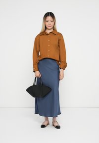 Brun langærmet skjorte med knapper ned foran, parret med en svajende blå maxi-nederdel. Sort struktureret taske og tofarget flade sko.