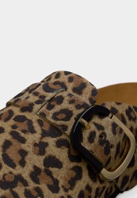 Chaussure mule imprimé léopard avec une surface texturée, dotée d'une bride à boucle noire et dorée. Forme arrondie avec une semelle douce de couleur neutre.