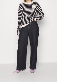 Pull en tricot rayé bleu marine et crème avec une accent floral, associé à un pantalon en denim large et foncé et des chaussures à talons blocs lavande.