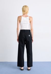 Black wide-leg jeans with a high waist and back pockets, worn with a white ribbed tank top. Setting features a plain background.