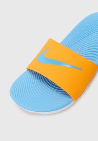Nike natikača s gornjim trakama u svijetlo narančastoj boji i platom. Ima teksturiranu površinu i utisnuti logo, što omogućava jednostavno stavljanje i skidanje.