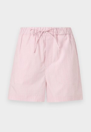 Femme portant un t-shirt rose à manches longues avec une poche poitrine et un short assorti, debout les mains dans les poches, sandales beiges sur fond blanc.