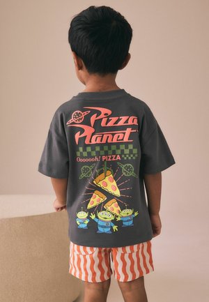 Kind trägt ein graues "Pizza Planet" T-Shirt mit Pizzastücken und drei grünen Außerirdischen, kombiniert mit orange-weiß gestreiften Shorts.