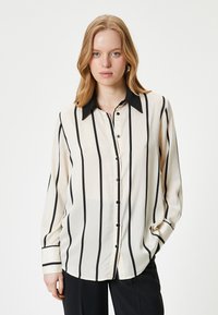 Beige blouse with black vertical stripes, a pointed collar, long sleeves, and button closure. Smooth fabric with glossy finish.