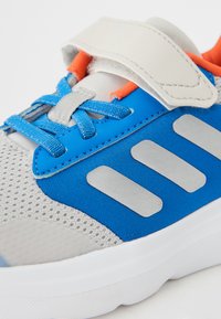 Baskets de sport bleues en matériaux mesh et synthétiques, avec des accents gris, une sangle Velcro et des détails orange. Semelle en caoutchouc.