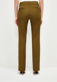 Olijfgroene slim-fit broek met een gladde textuur, twee achterzakken en een op maat gemaakte tailleband, gecombineerd met zwarte hoge hakken.