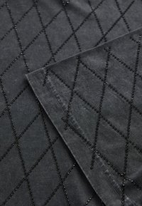 Tessuto nero con un motivo a diamante formato da piccole perline nere; due strati sovrapposti, che mostrano una texture liscia e una cucitura precisa.