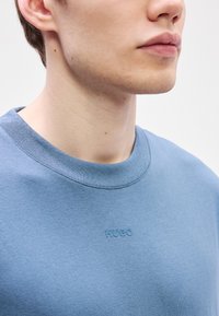 Ανοιχτό μπλε φούτερ με στρογγυλή λαιμόκοψη, που διαθέτει μια διακριτική λογότυπη "HUGO", κατασκευασμένο από μαλακό, υφαντό ύφασμα με ραμμένες λεπτομέρειες στη λαιμόκοψη.