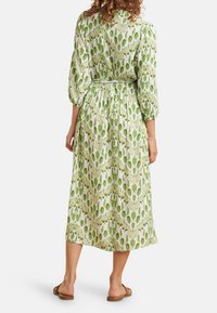 Grün-weiß gemustertes Midi-Kleid mit Puffärmeln und tailliertem Schnitt, gefertigt aus leichtem Stoff. Getragen mit flachen Sandalen.
