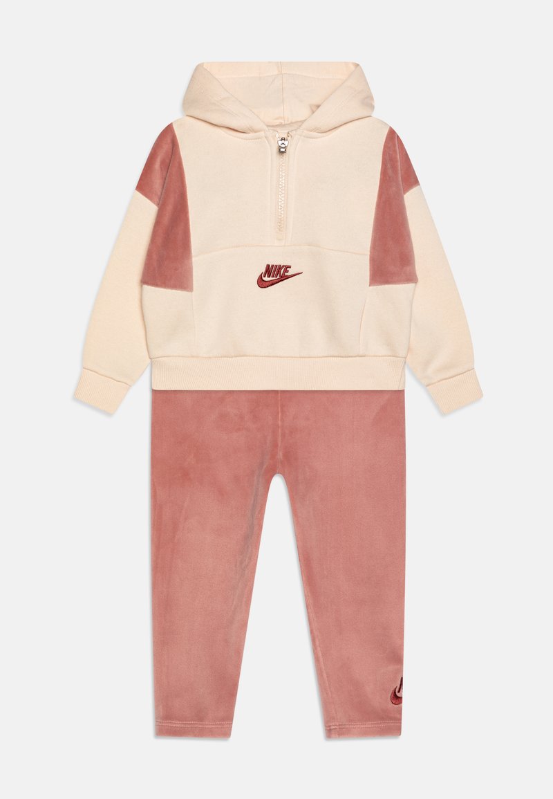 Tuta con zip, con cappuccio a due tonalità in velluto crema e rosa, caratterizzato da un piccolo logo Nike rosso sul petto e sulla gamba, con dettagli a pannello a contrasto.