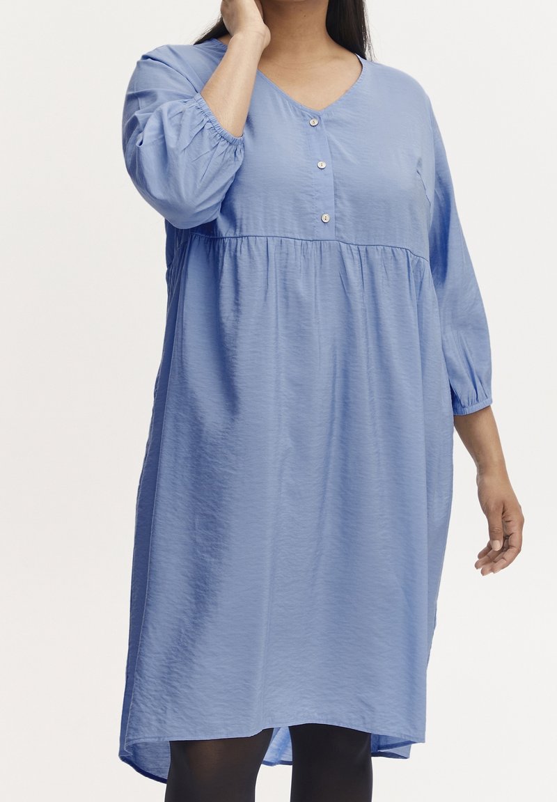 Robe midi bleue en tissu léger, avec un col en V, des manches trois-quarts et trois boutons décoratifs à l'avant. Texture douce, coupe décontractée.