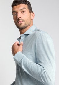 Lichtblauwe lange mouwen polohemd met een knoopsluiting kraag, gemaakt van een zachte, gestructureerde stof en een subtiel gemêleerd patroon.