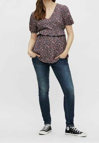 Top a maniche corte con scollo a V e motivo floreale, con vita aderente; abbinato a jeans skinny scuri e sneakers alte nere.