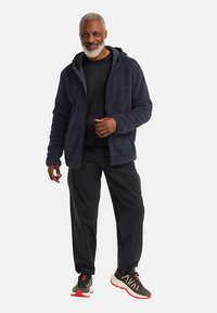 Navy fleece zip-up jacket with a hood, paired with a black shirt and black pants. Features pockets and a textured fabric. Shoes with accents.