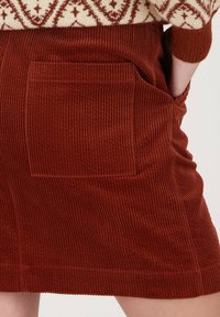 Jupe en velours côtelé marron avec des côtes verticales, une poche arrière et une coupe droite, en tissu texturé et doux.