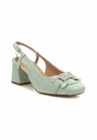 Zapato de terciopelo verde con tacón cuadrado, que presenta un bonito lazo brillante y un pequeño charm en la correa del tobillo.