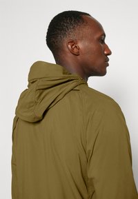 Olive green hooded jacket made of lightweight fabric, featuring a smooth texture and a minimalist design with no visible logos or patterns.