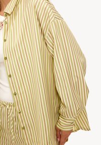 Persona que lleva una camisa de rayas verticales verdes y blancas de corte holgado con mangas abullonadas y pantalones a rayas a juego atados en la cintura.