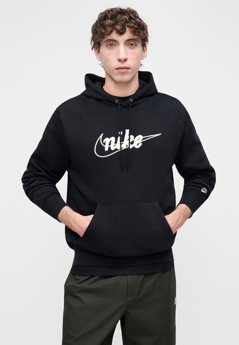 Black cotton hoodie with a front kangaroo pocket, featuring a large white Nike logo. Ribbed cuffs and hem with an adjustable drawstring hood.