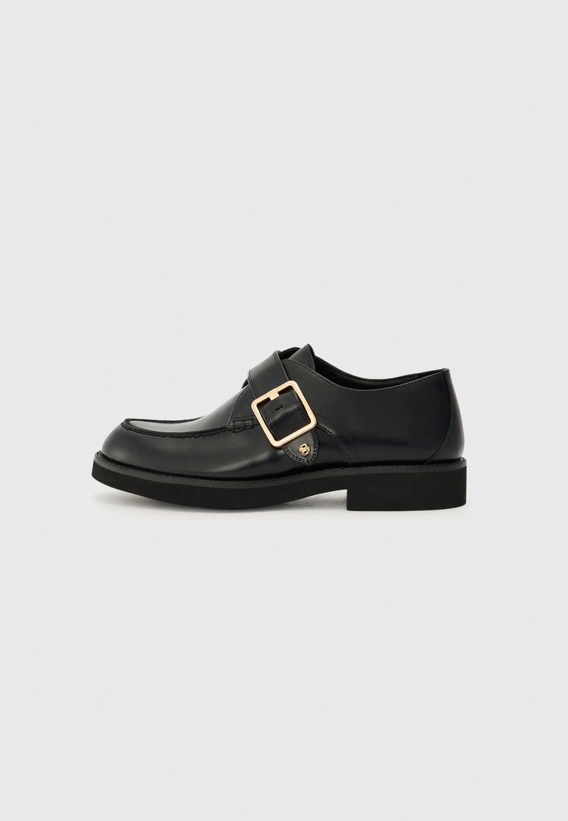 Black leather shoe with a rounded toe, featuring a gold buckle and a flat rubber sole. Smooth texture with subtle stitching details.