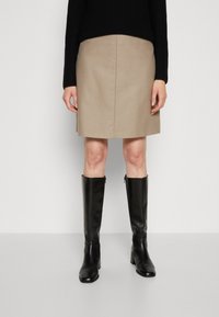 Beige wollen rok in een mix van materialen, tot aan de knie, gecombineerd met hoge zwarte leren laarzen met hak. De rok heeft een schone, gladde uitstraling zonder versieringen.