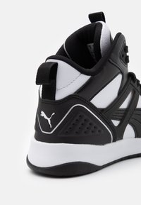 Černo-bílé sportovní boty s texturovaným svrškem, polstrovaným límcem, gumovou podrážkou a výrazným logem na patě a boku.