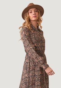Vestido de mangas largas, estampado en colores oscuros con diseños florales y geométricos. Presenta un cuello y una cintura ceñida, con una falda fluida.
