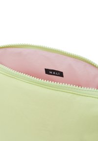 Bolsa con cremallera en verde claro con una textura suave, con un interior rosa y una etiqueta negra que dice "NALÍ."