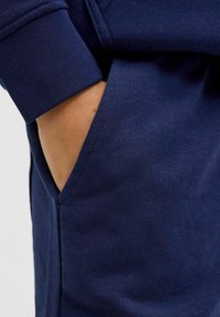 Felpa blu navy con polsini a costine e tasca laterale. Il tessuto presenta una texture liscia con dettagli di cucitura sottili.