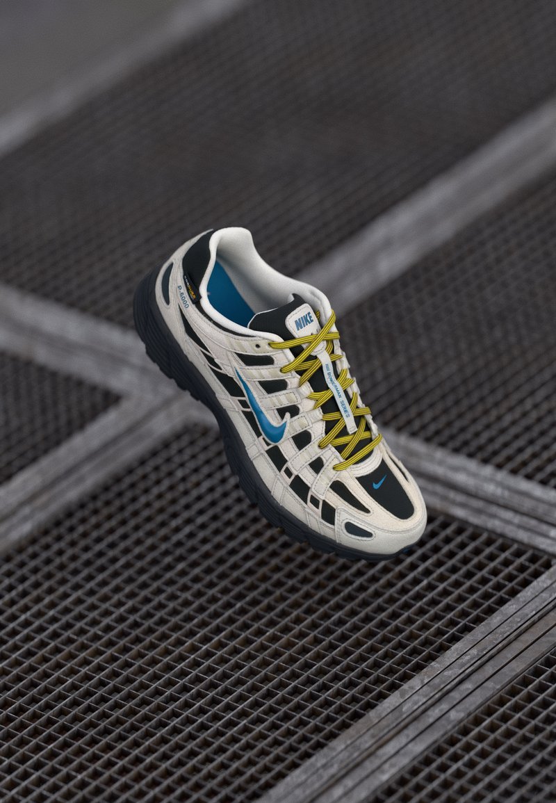 Baltās un melnās Nike skriešanas kurpes ar zilu Swoosh un dzeltenām šņorēm, izstādītas uz tumšas metāla režģa virsmas.