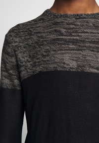 Dzianinowy sweter z gradientowym wzorem od ciemnoszarego u góry do jednolitego czarnego na dole. Teksturowana tkanina z okrągłym dekoltem.