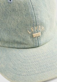 Light blue denim cap with curved brim featuring embroidered "Levi's" logo in cream thread on the front panel.