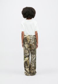 Biele tričko s krátkym rukávom v kombinácii so širokými nohavicami s textúrovaným vzorom hnedo-zeleného maskáča, pohľad zozadu.