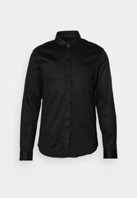 Chemise noire à manches longues avec col, boutons cachés sur le devant et poignets boutonnés sur un fond clair uni.