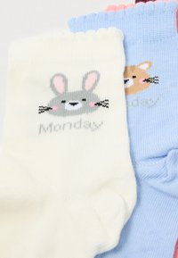 Tre par børnestrømper: hvide med en grå kanin og "Mandag", lyseblå med en brun kanin, ribbet tekstur, bølgede kanter.