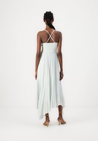 Gai pastelu zaļš maksi kleita ar spageti siksnām, smalcinātu jostu un plūstošu svārku. Iezīmējas ar asimetrisku apakšmalu un delikātu tekstūru.