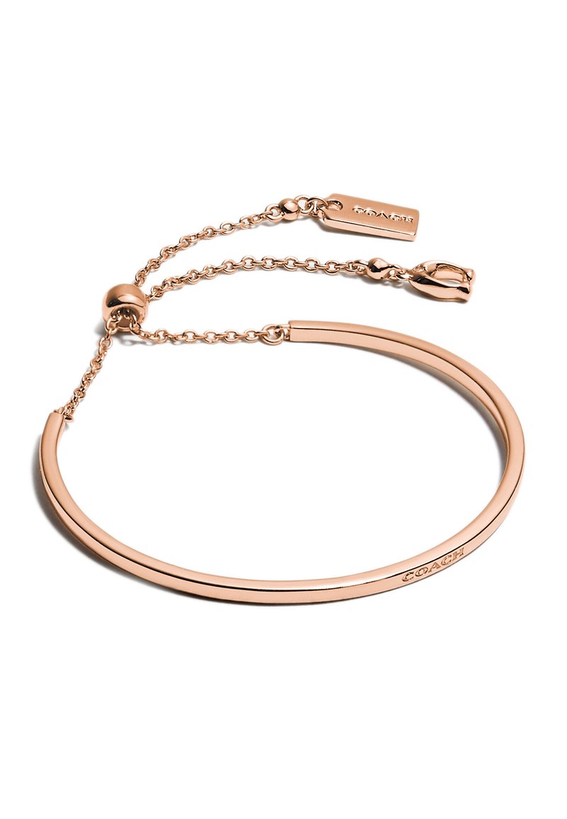 Pulsera de metal color dorado rosado con forma suave y redondeada. Cuenta con una cadena ajustable y una etiqueta con texto grabado.