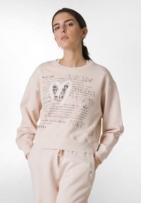 Jasnoróżowy, krótki sweatshirt wykonany z miękkiego materiału, z teksturowanym wzorem serca i tekstem związanym z baletem w różnych czcionkach.