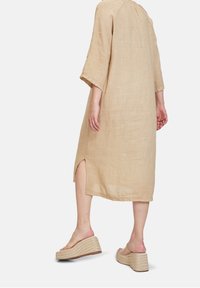 Beige liinapuku, jossa on kolme neljänneshihaa ja sivuhalkioita. Yhdistetty kudottujen alustossujen kanssa, joissa on paksu pohja.