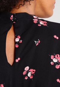 Black fabric with a floral print in pink and white; features a keyhole back design with two black buttons at the neckline.