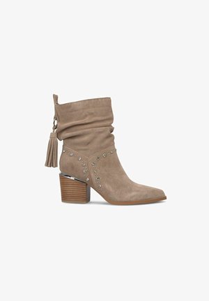 Bottine en suede beige avec tige tombante, ornements en strass, accents argentés et talon en bois épais. Détails en franges.