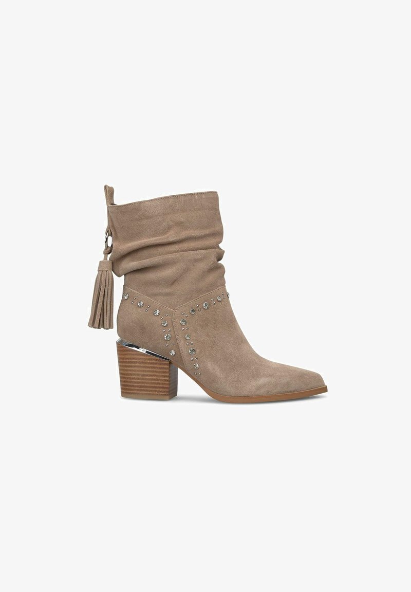 Beżowe zamszowe botki za kostkę z luźną cholewką, dekoracyjnymi kryształkami, srebrnymi akcentami i masywnym drewnianym obcasem. Zawierają detal w postaci frędzli.