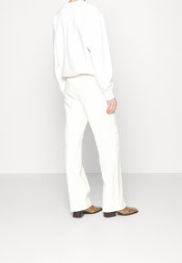 Vit långärmad topp i kombination med figurnära vita byxor. Bruna mönstrade skor fulländar outfiten. Minimalistisk stil med en ren design.