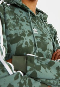 Green tie-dye hoodie made of soft fabric, featuring a lined hood, white drawstrings, and contrasting white stripes along the sleeves.