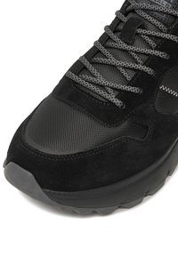 Melns sporta apavu pāris ar zīdu un tīkliņa materiālu kombināciju, teksturētu virsmu, pelēkām auklām un biezu gumijas zolīti ar nelielu izliekumu.