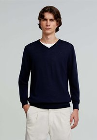 Pulover de marin cu guler în V, din tricot ușor. Are mâneci lungi și tiv ribbit. Purtați-l peste o cămașă albă, cu un detaliu subtil al logo-ului pe piept.